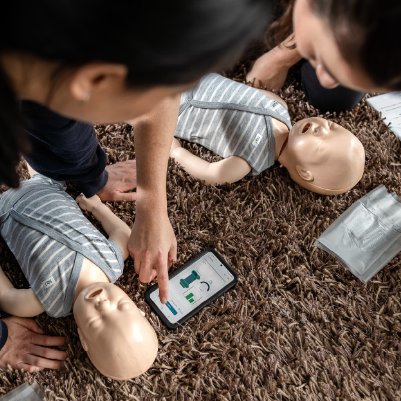 Two people practicing CPR on mannequins with a smartphone displaying instructions.