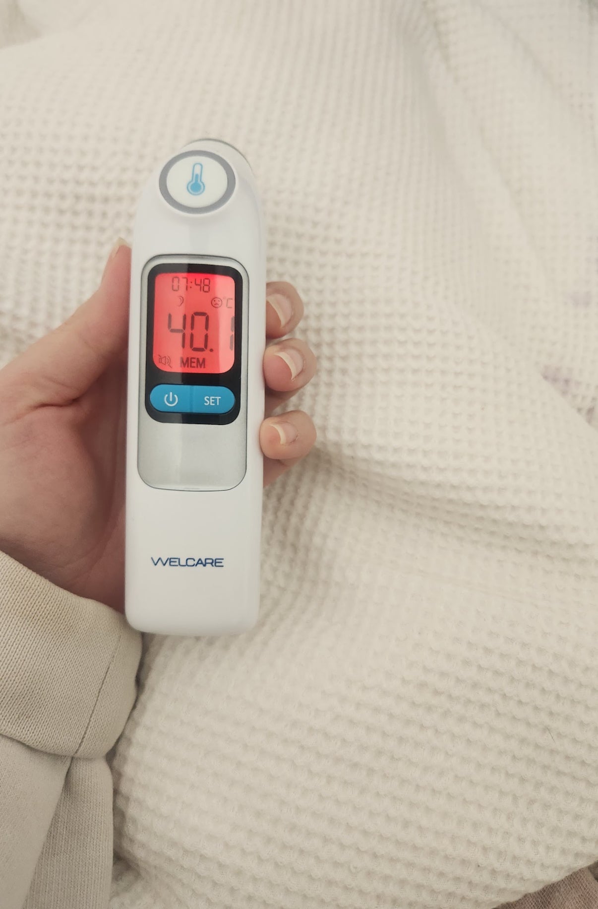Digital thermometer held by a person with a beige background