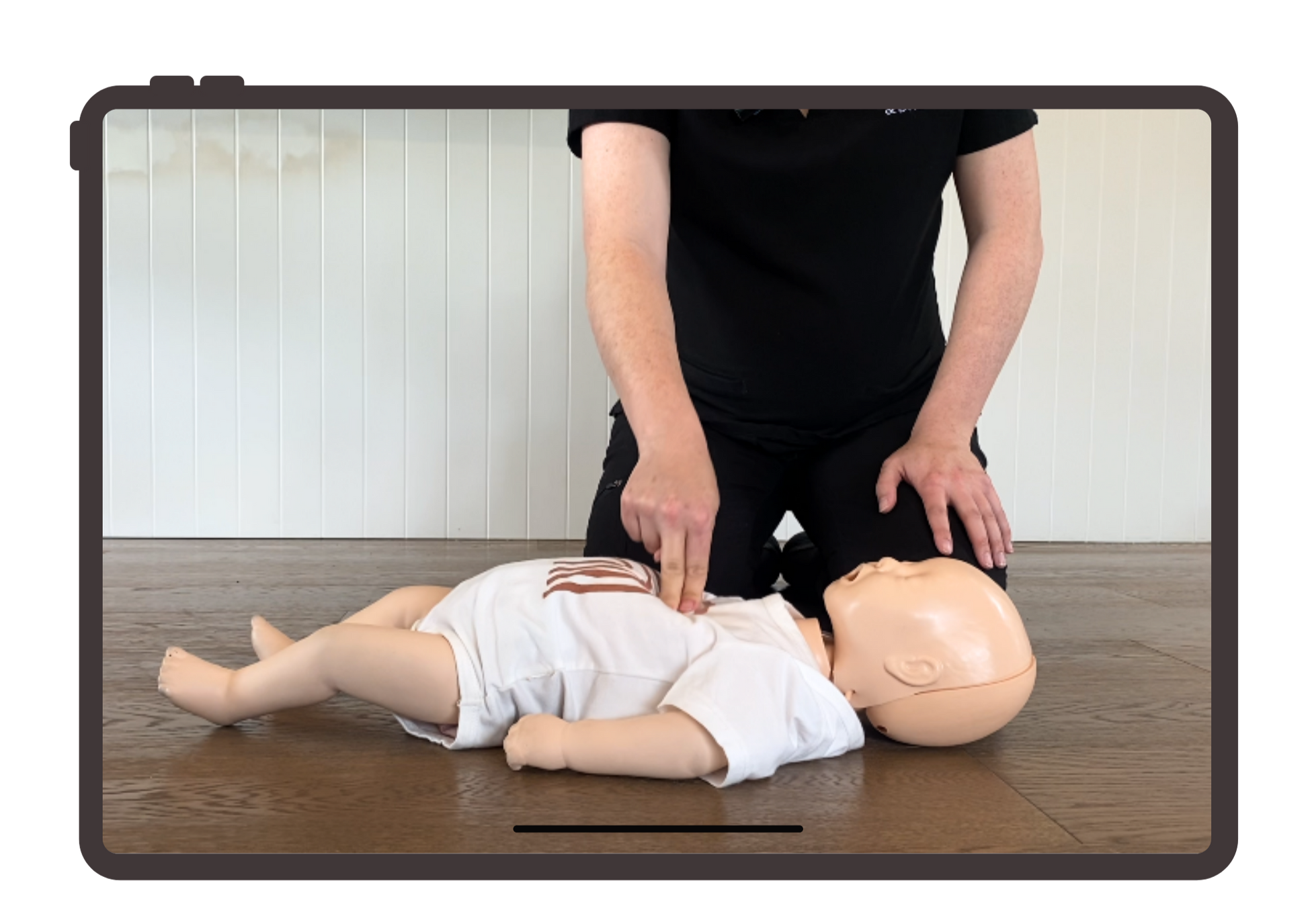 Person demonstrating CPR on a mannequin using a tablet device.
